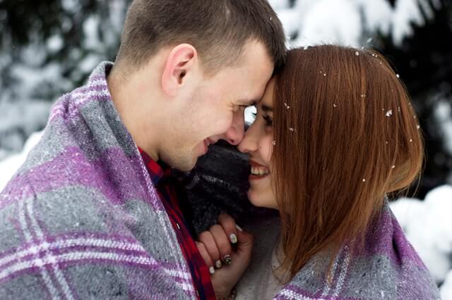 Two people cuddled in a blanket outside during a winter date. You'll love these date ideas for couples.