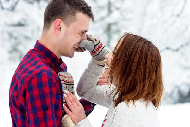 Woman pinching guys nose outside while dating in the winter. 